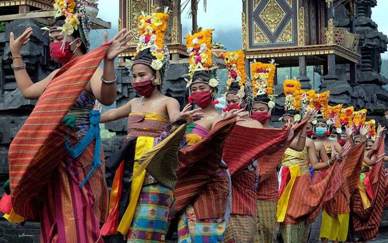 Balinese traditional dancers wearing colorful costumes and face masks during a temple ceremony, following Wear Mask or Get Fined regulations in Bali.