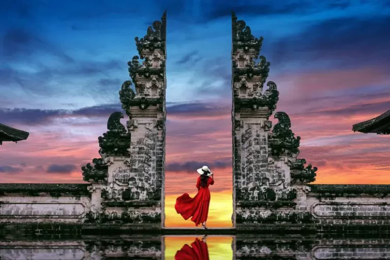 Traveler in red dress posing at the famous Gates of Heaven, one of The Most Instagrammable Places in Bali, with a stunning sunset sky and temple reflection.