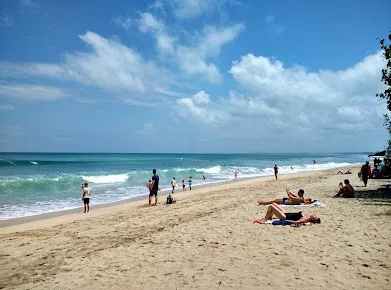 Kuta Beach view with tourists relaxing under umbrellas and enjoying sunny weather, featured in Bali tour packages for beach lovers.