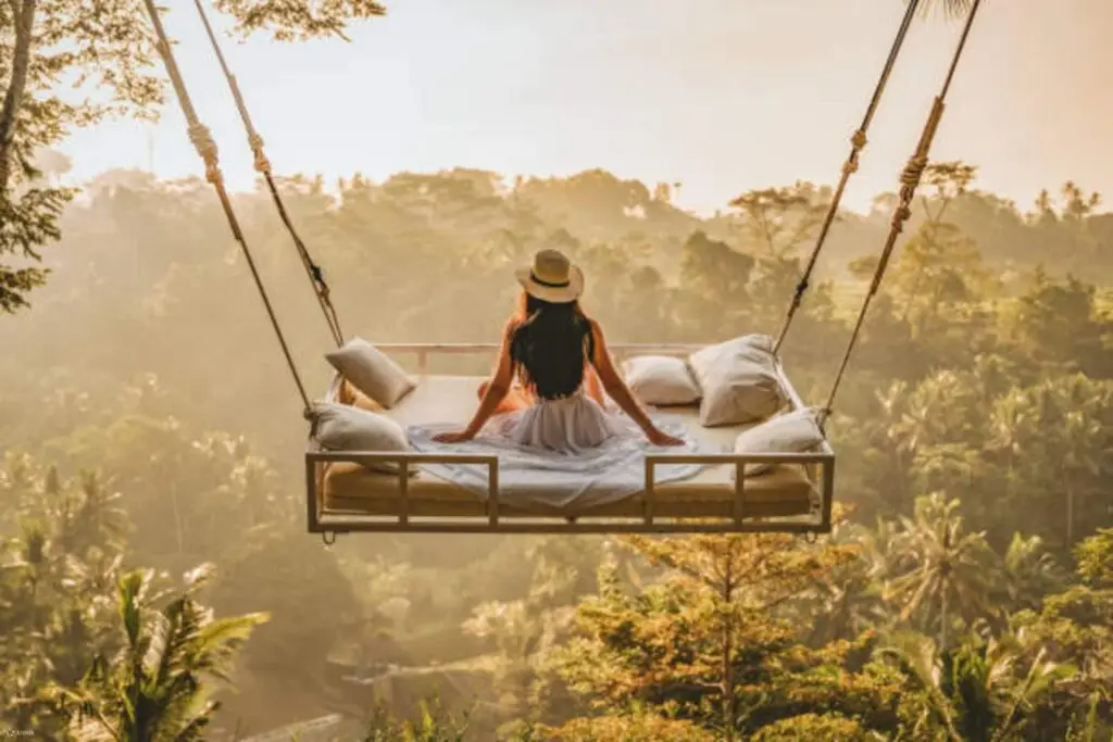 Woman relaxing on a hanging swing bed at sunrise during her Flexible Bali Tour.